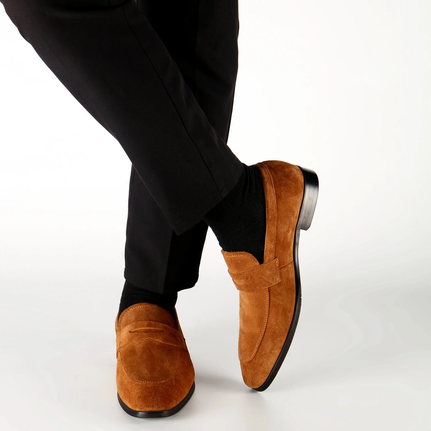 Brown suede loafers worn with black pants on a white background