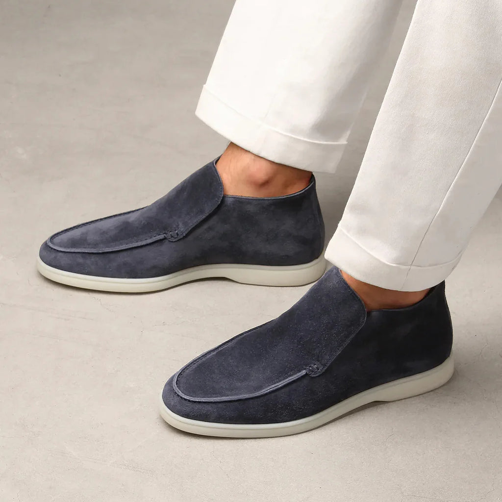 Navy loafers worn with white pants on a neutral background