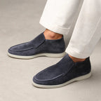 Navy loafers worn with white pants on a neutral background