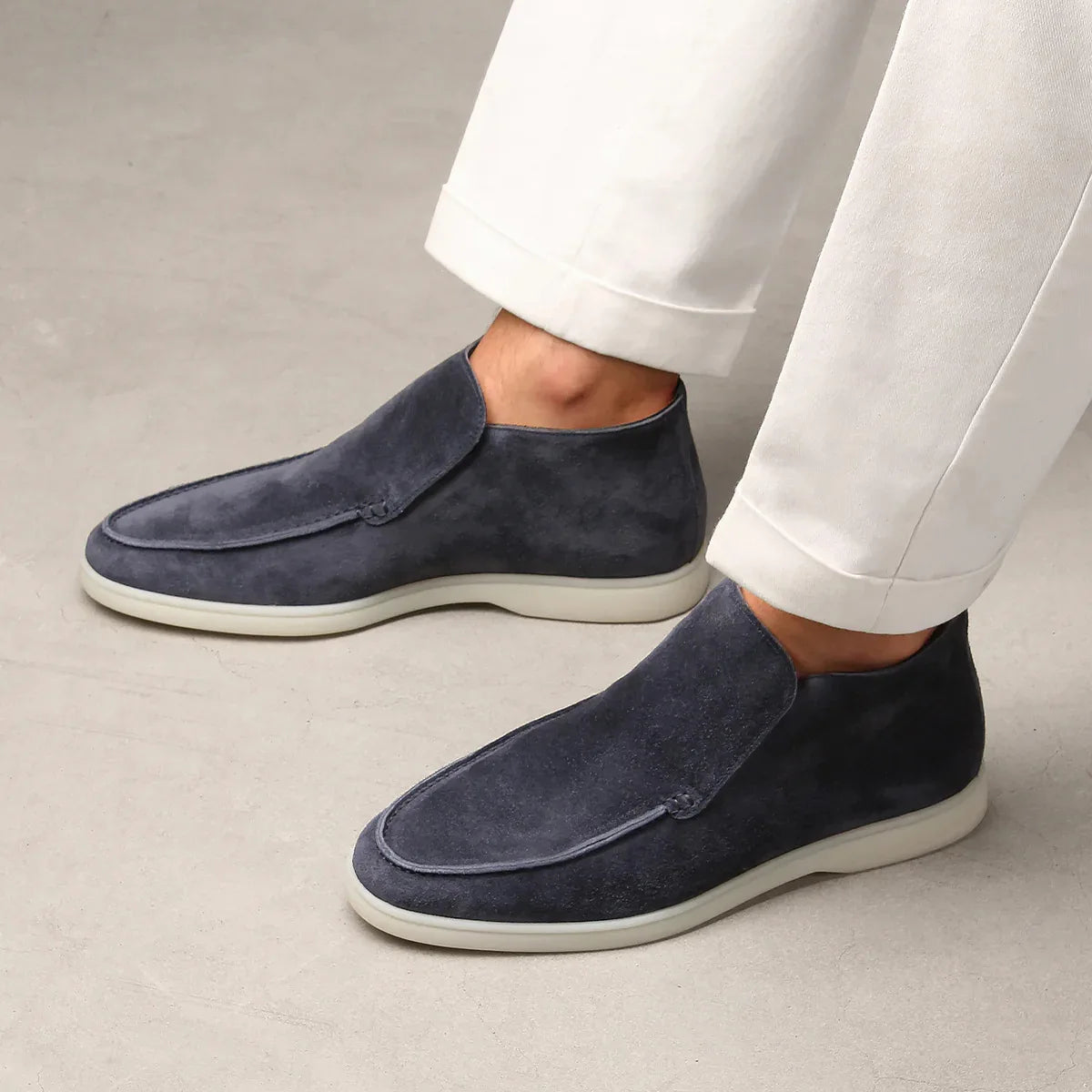 Navy loafers worn with white pants on a neutral background