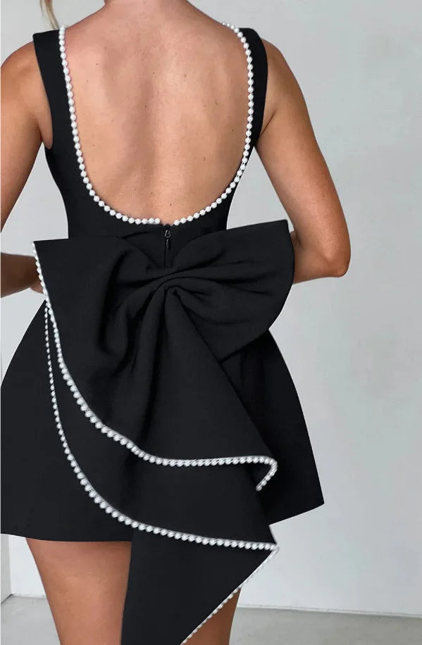 Black dress with a large bow and pearl trim on a plain background