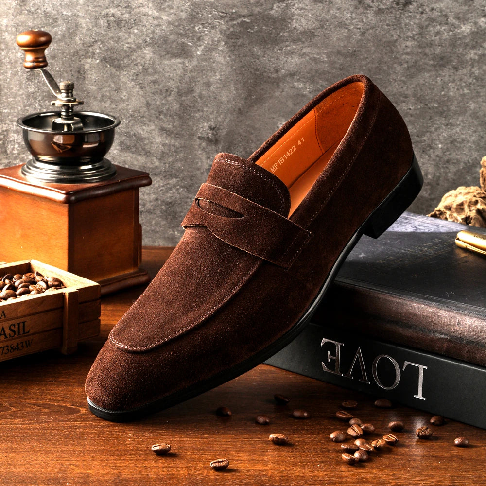 Brown suede loafer shoe on a wooden surface with coffee beans and a grinder.