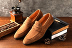 Brown suede loafers on a wooden surface with coffee beans and a grinder.