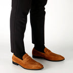 Brown loafers worn with black pants on a white background
