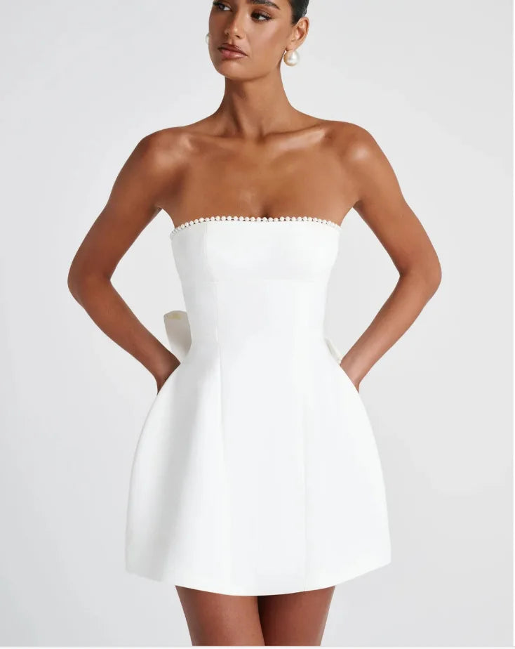 Woman wearing a white strapless dress with ruffled details on a plain background