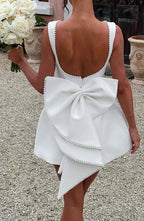 White dress with a large bow detail on the back, held by a person outdoors.