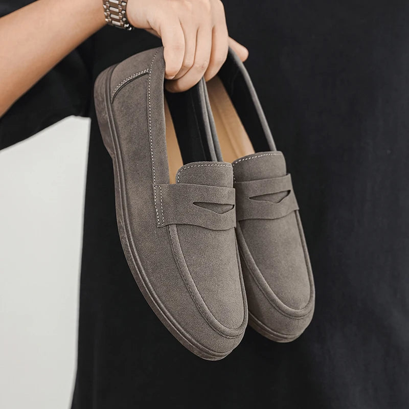 Pair of gray loafers held by a person against a black background