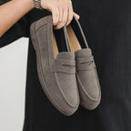 Pair of gray loafers held by a person against a black background