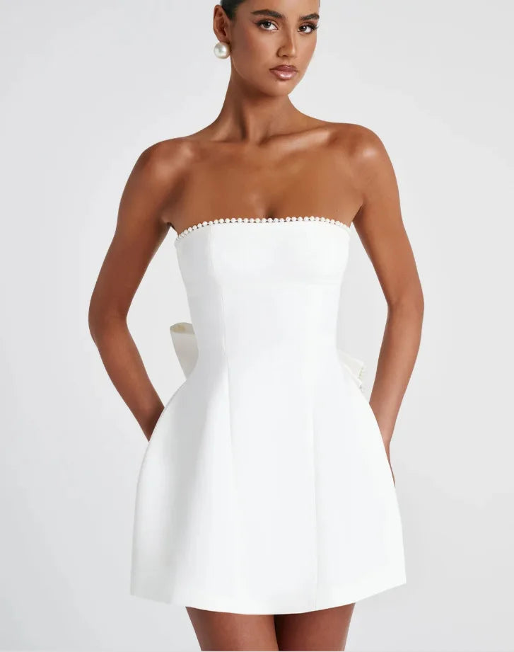Woman wearing a strapless white dress with pearl details on a white background