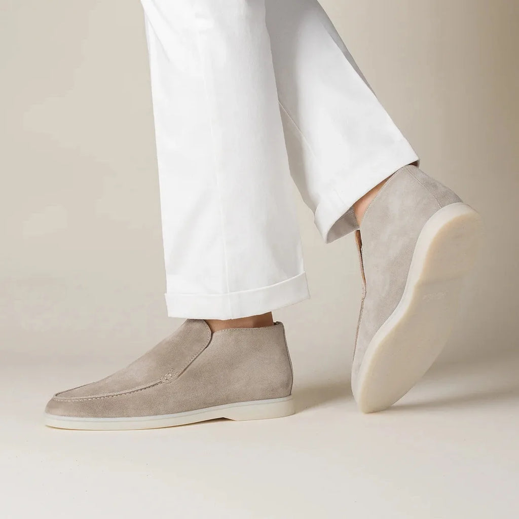 Beige slip-on shoes worn with white pants on a neutral background
