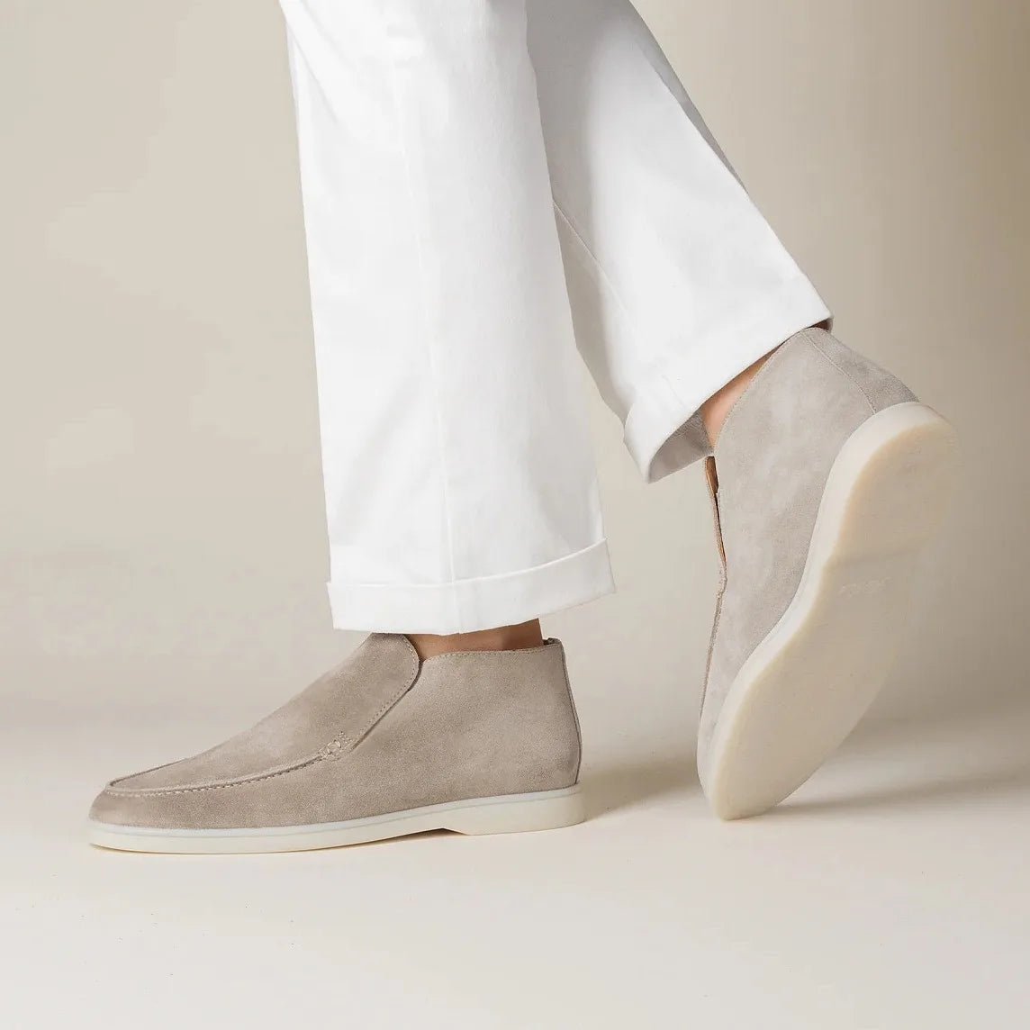 Beige slip-on shoes worn with white pants on a neutral background