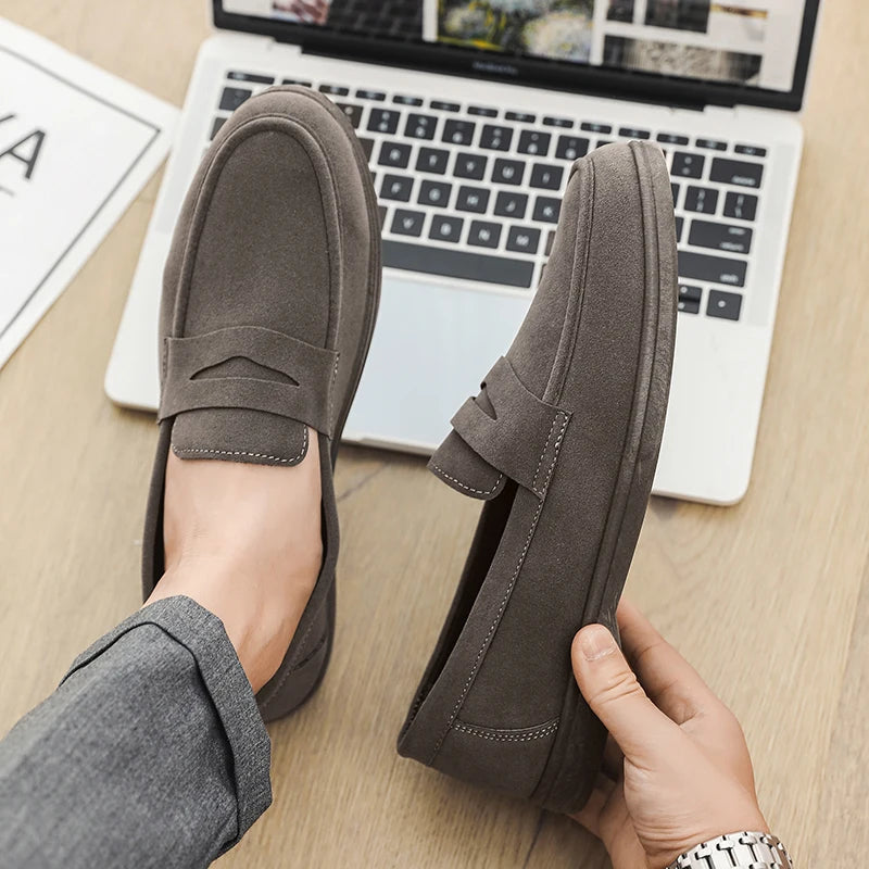 Person wearing brown loafers with a laptop on a desk