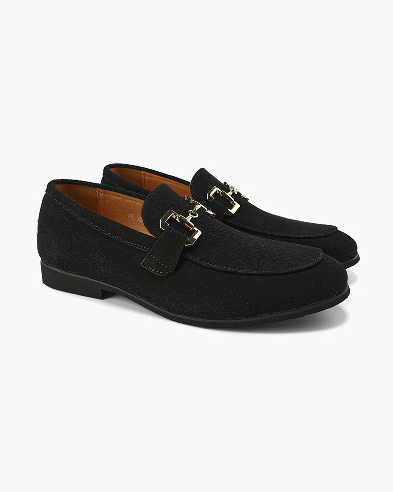 Pair of black suede loafers with gold buckles on a white background