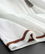 Close-up of a white sweater with brown ribbed pattern on a dark surface