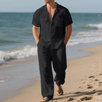 Man wearing a black jumpsuit walking on a beach with ocean waves in the background