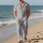 Man in a gray jumpsuit standing on a beach with ocean waves in the background