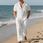 Man in a white outfit standing on a beach with ocean waves in the background