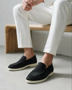 Person wearing black loafers and white pants sitting on a wooden bench.