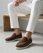 Brown loafers worn with white pants on a neutral background