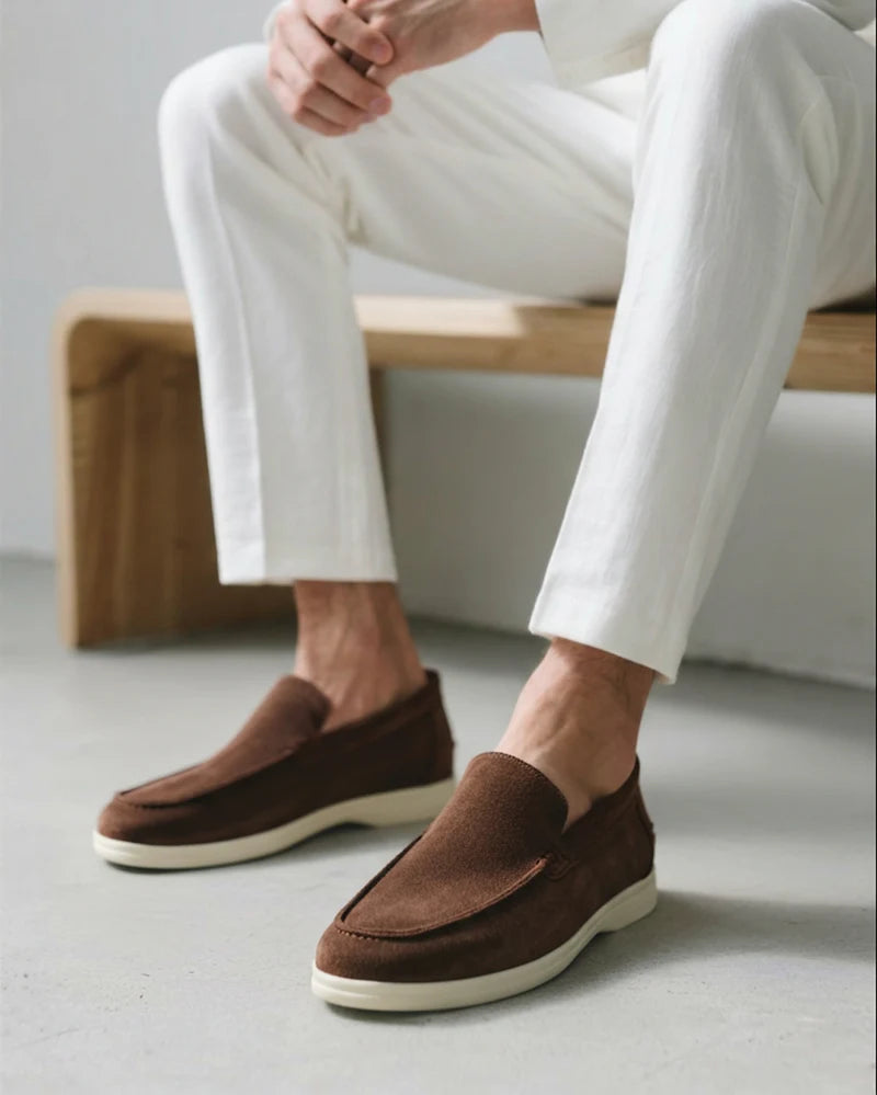 Brown loafers worn with white pants on a neutral background