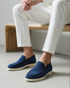 Person wearing blue loafers and white pants sitting on a wooden bench.