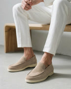 Person wearing beige loafers and white pants sitting on a wooden bench.