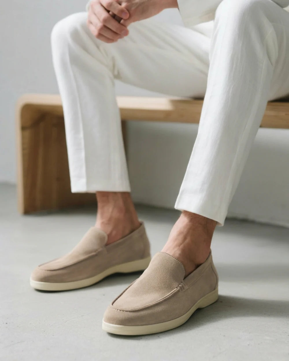 Person wearing beige loafers and white pants sitting on a wooden bench.