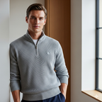 Man wearing a gray sweater with a small logo, standing indoors.